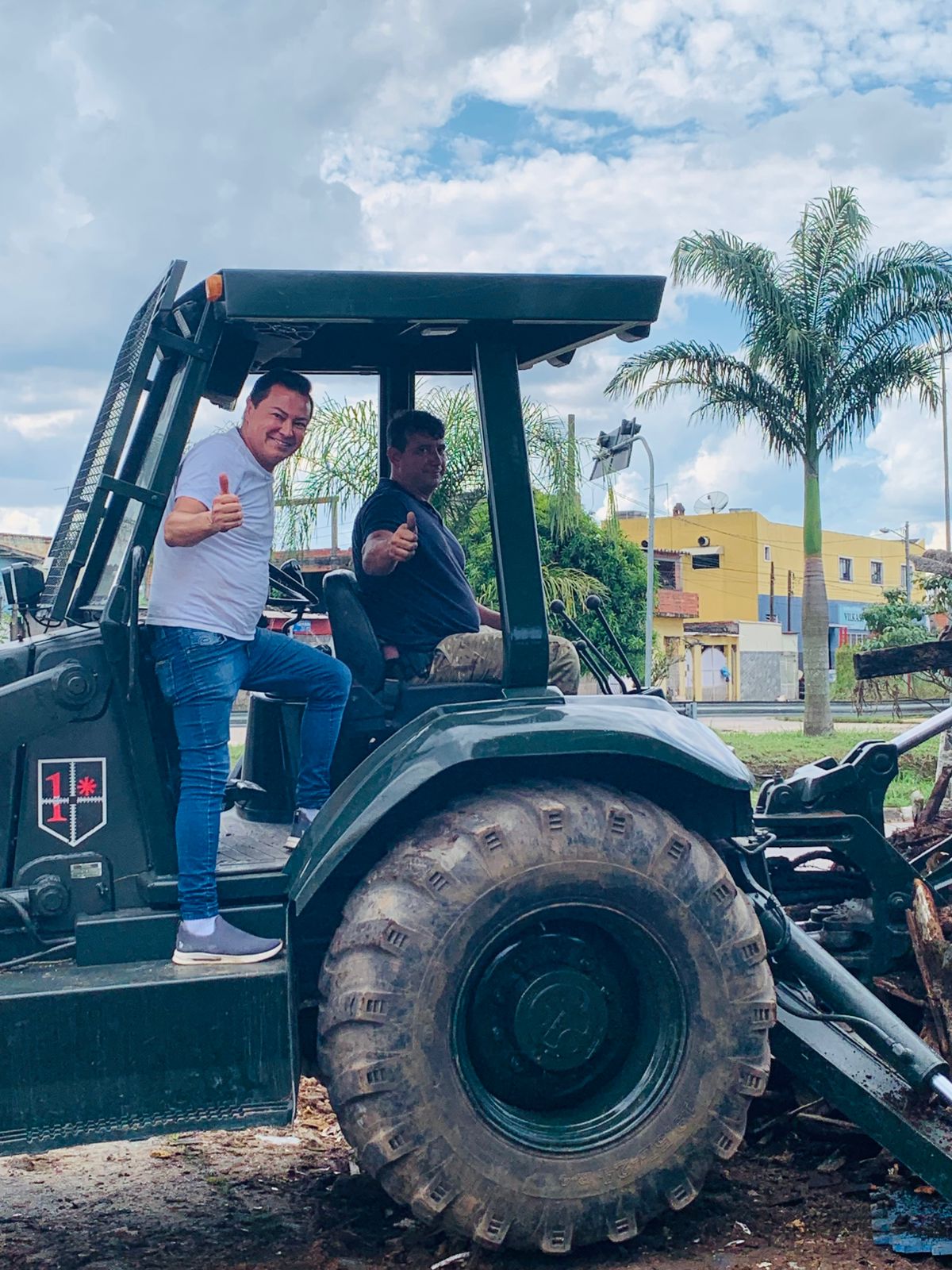 vereadores Marcel da ONG (à frente, de pé em veículo que faz limpeza em via, de camiseta branca) e Adilson Horse (sentado, pilotando o equipamento) fazem sinal de positivo.