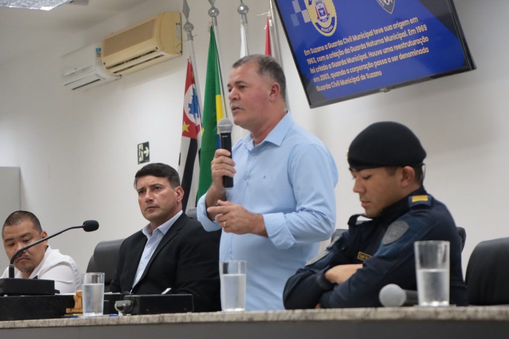 De pé, na Mesa Diretiva da Câmara de Suzano, secretário de Segurança Cidadã Francisco Balbino fala ao microfone. Sentados, da esquerda para a direita, estão o assessor estratégico Marcelo Miyazaki, o vereador Adilson Horse e o comandante da Guarda Civil Municipal Rodrigo Kanashiro.