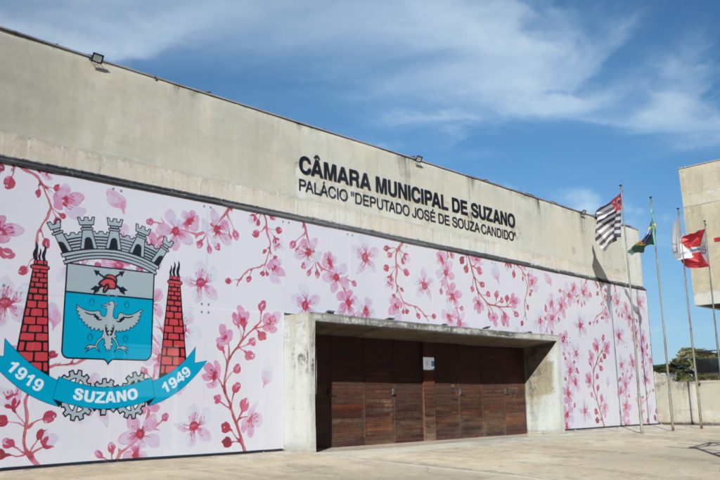 Fachada da Câmara de Suzano, com ilustrações de flores de cerejeira em vários tons de rosa e um brasão do município adesivados.
