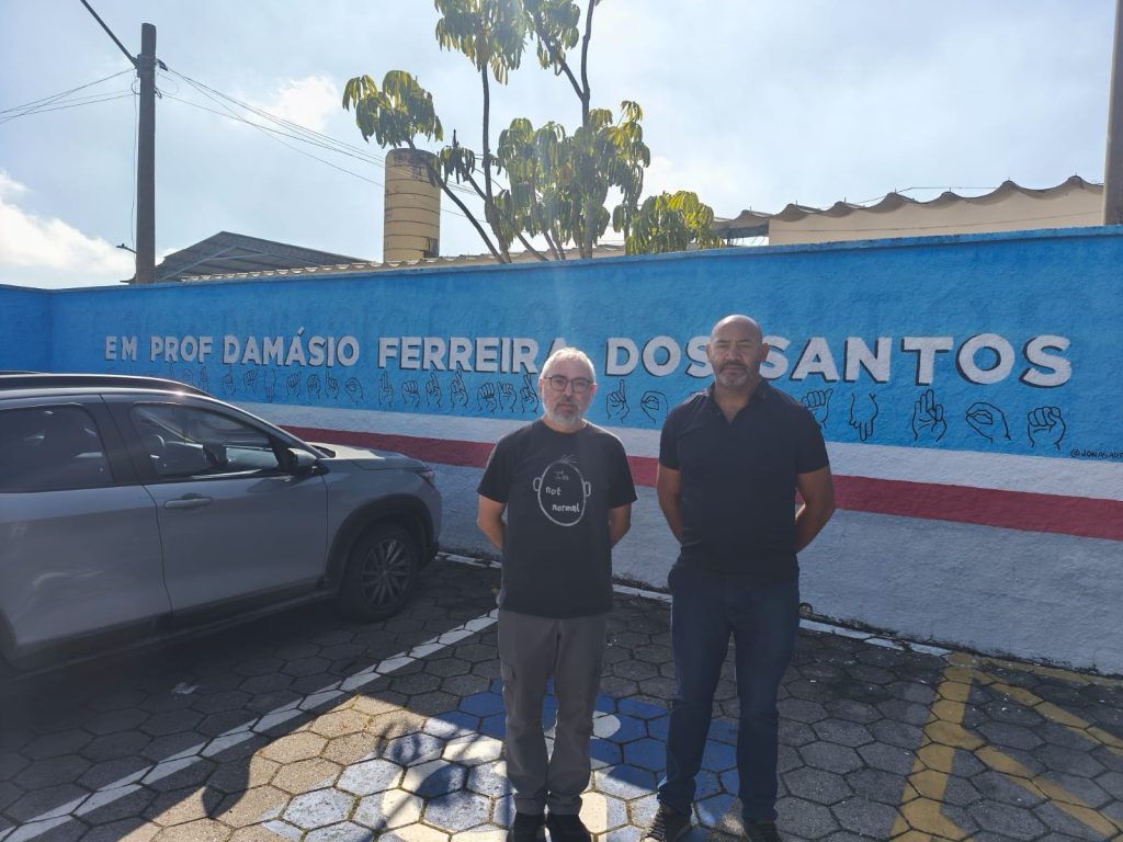 De pé, em frente ao muro da escola, estão, da esquerda para a direita, o diretor Marco Maida e o vereador João Sabugo.