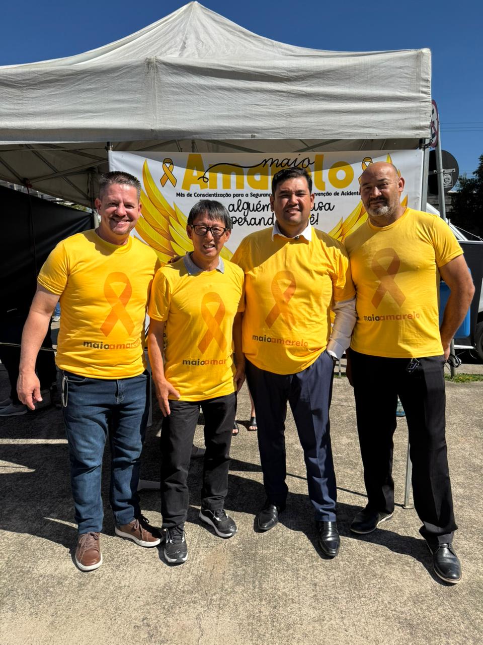 Lado a lado, da esquerda para a direita, estão vereador Maizena, vereador Artur Takayama, prefeito Pedro Ishi e vereador João Sabugo. Todos usam camiseta amarela da campanha Maio Amarelo.