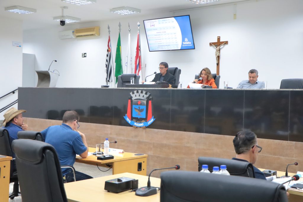 De costas, vereadores sentados em suas mesas no Plenário. Na Mesa Diretiva, estão, da esquerda para a direita, Artur Takayama, a diretora jurídica da Saúde, Tânia Porfírio, e o  diretor de Especialidades André Moraes em audiência realizada em 27 de fevereiro.