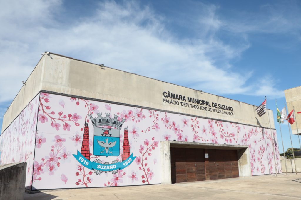 Fachada da Câmara de Suzano, com ilustração adesivada de flores de cerejeira em vários tons de rosa e o brasão do município.