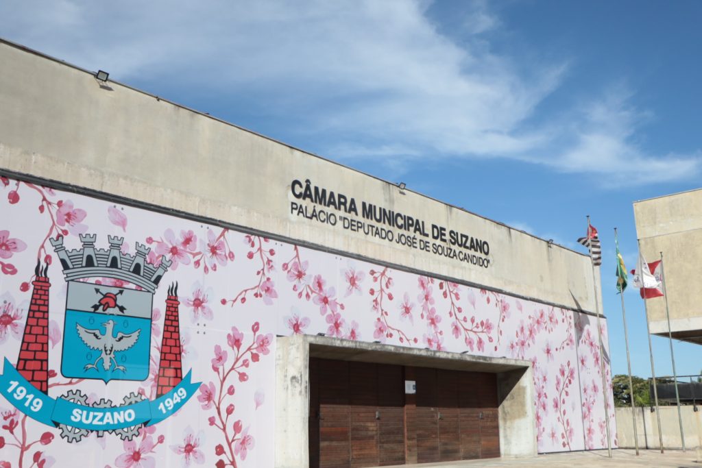 Fachada da Câmara de Suzano, adesivada com ilustrações de flores de cerejeira em vários tons de rosa e o brasão do município.