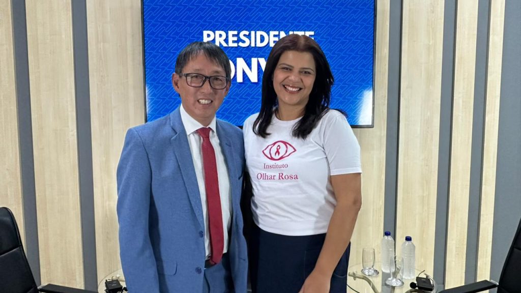 De pé, no estúdio da TV Câmara, Artur Takayama e Fabiana Fernandes posam para foto lado a lado.