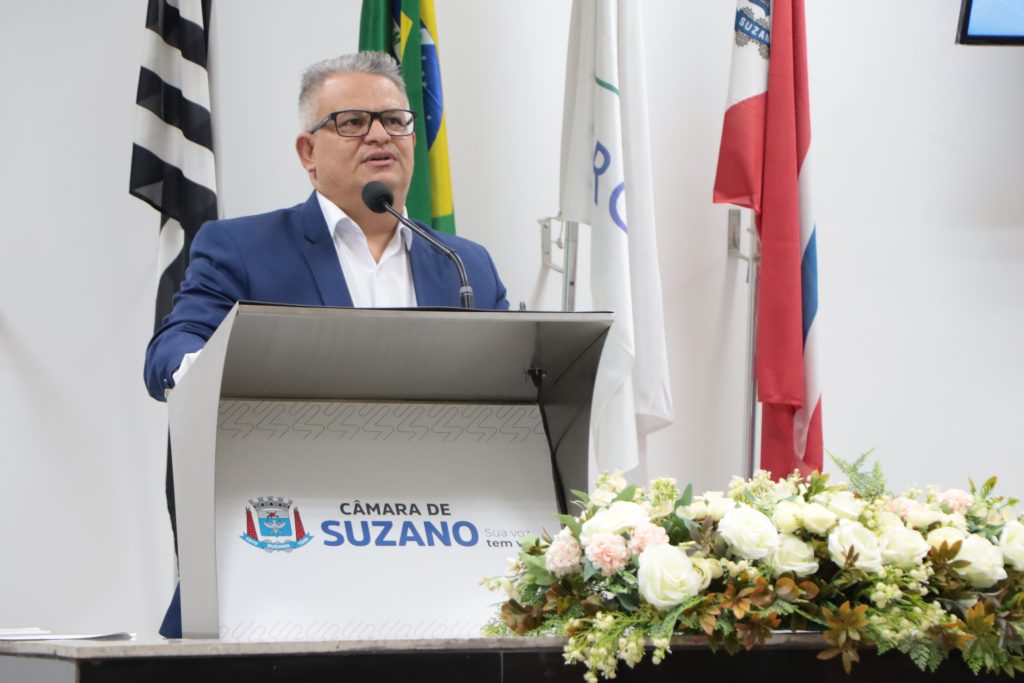 Vereador professor Edirlei fala ao microfone na Tribuna da Câmara. Ele usa blazer azul e camisa social branca.