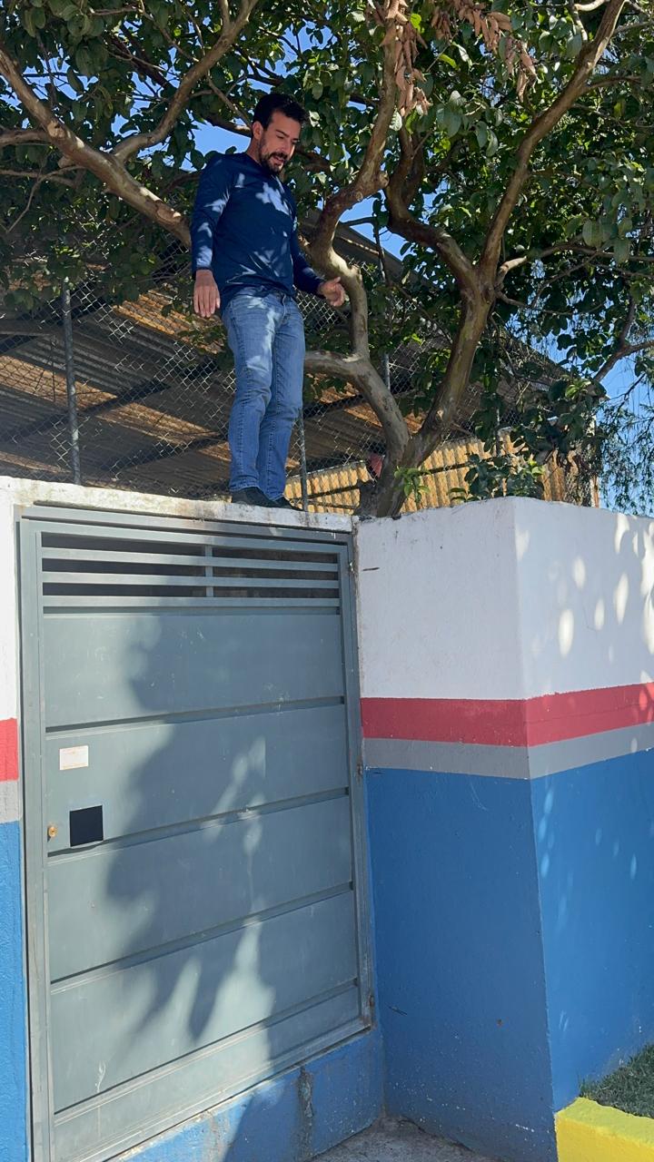Vereador Marcio Malt, de pé, em cima de muro de escola. Ele usa calça jeans e camisa social azul.