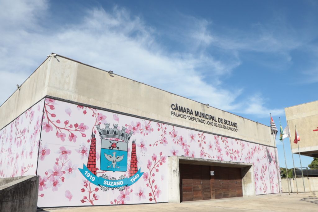 fachada da Câmara de Suzano, adesivada com ilustração de flores de cerejeira em diversos tons de rosa e o brasão do município.