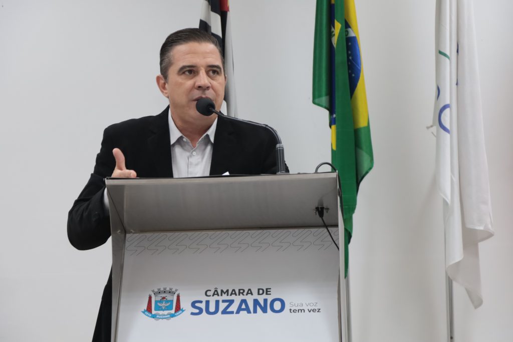 vereador Leandrinho fala ao microfone na Tribuna da Câmara. Ele usa camisa social clara e blazer preto.